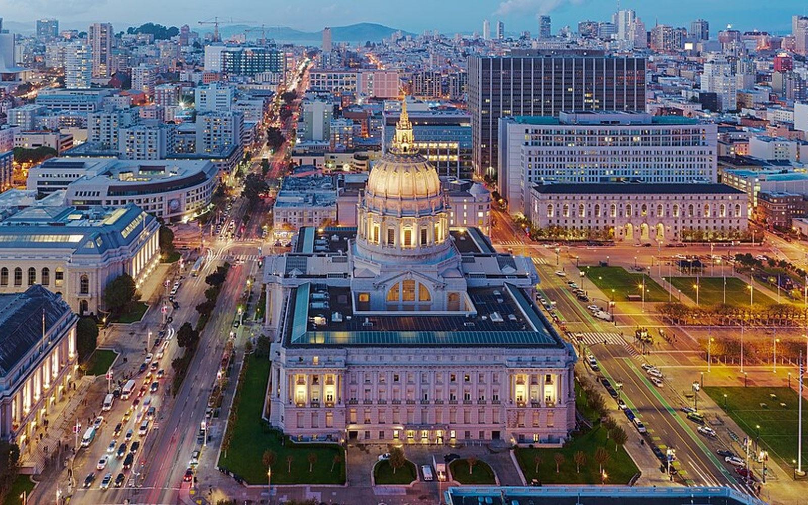 Aerial view of San Francisco City Hall's illuminated dome amid the surrounding cityscape at dusk